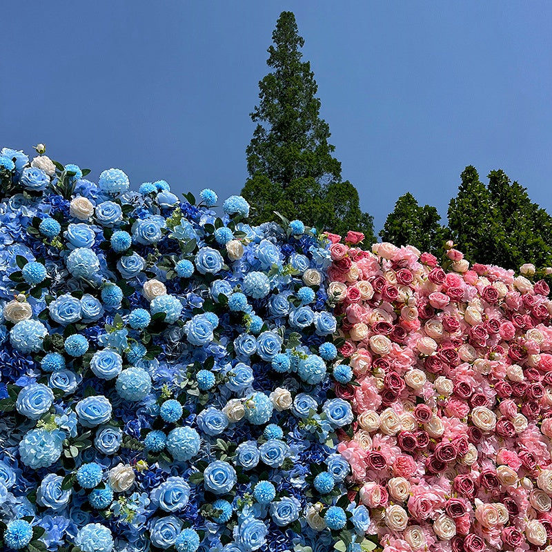 Two large floral arrangements, one blue and one pink, against a clear blue sky with trees in the background.