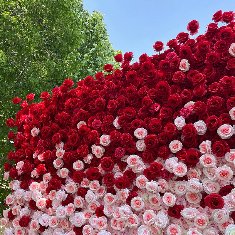 Large arrangement of red and pink roses against a blue sky with green trees.